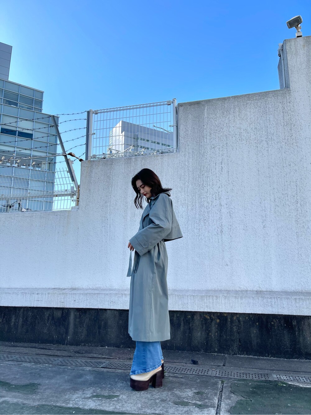 グリーン系のトレンチコート、ホワイト系のサンダル、ブルー系のデニムパンツを着用したレディースの冬コーディネートの2枚目の写真