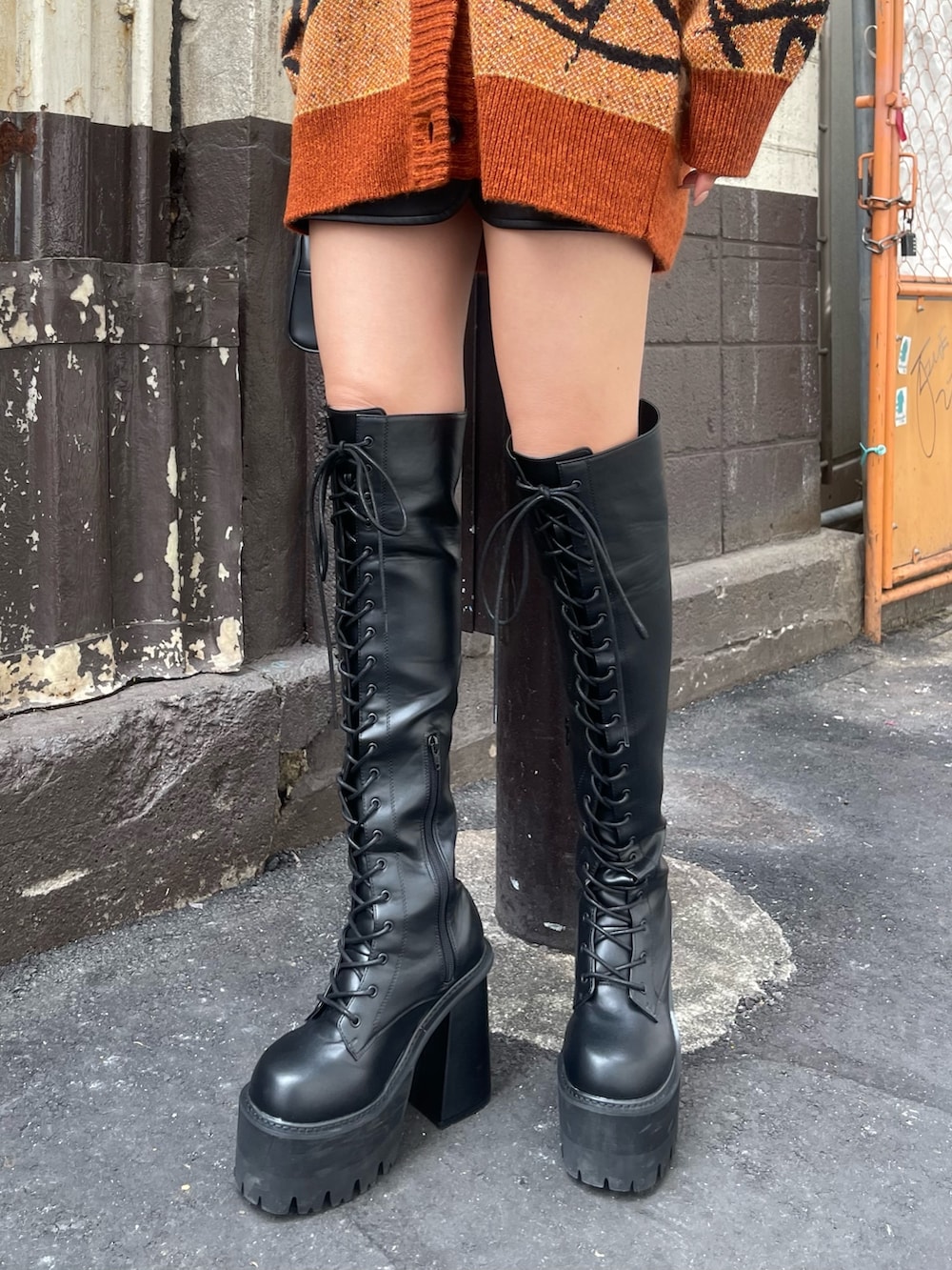 オレンジ系のニット/セーター、ブラック系のハンドバッグ、ブラック系のブーツを着用したレディースの秋コーディネートの7枚目の写真