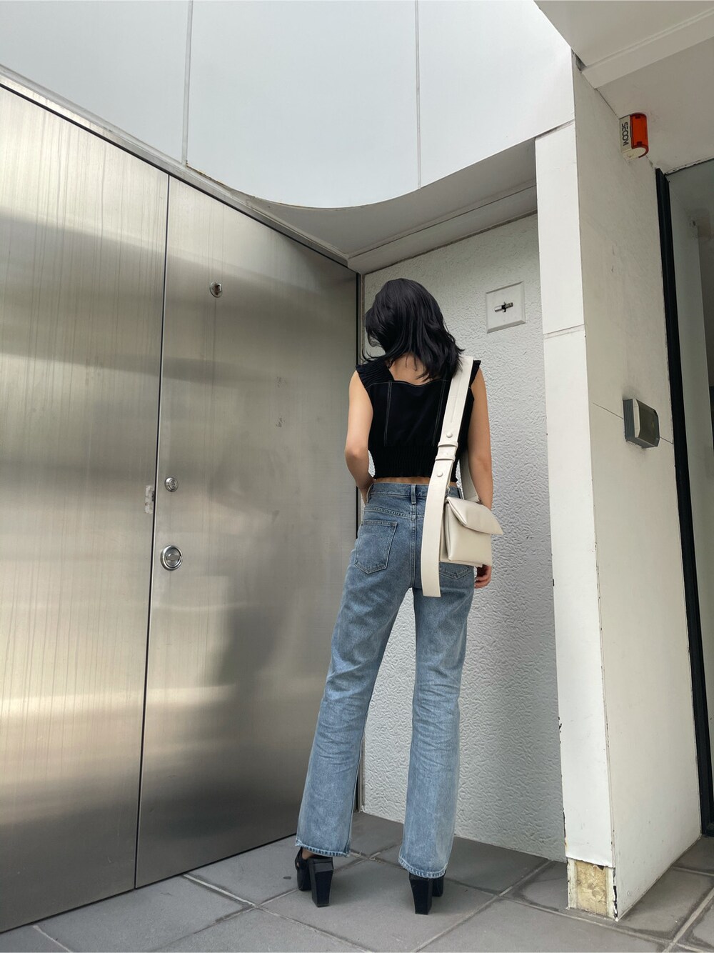 ホワイト系のショルダーバッグ、ブラック系のサンダル、ブルー系のデニムパンツを着用したレディースの春コーディネートの2枚目の写真