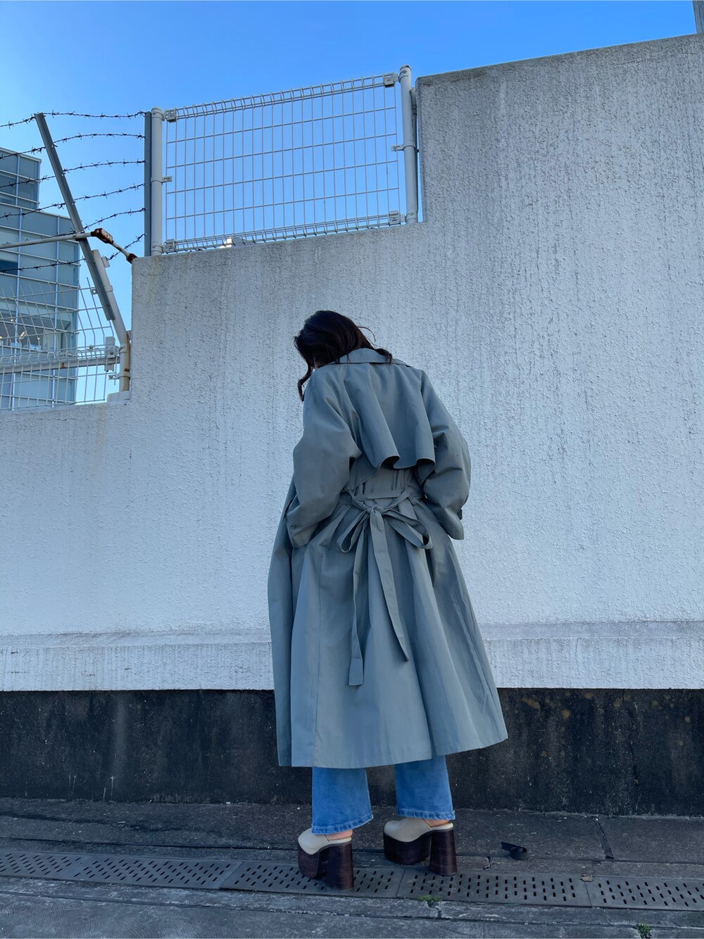 グリーン系のトレンチコート、ホワイト系のサンダル、ブルー系のデニムパンツを着用したレディースの冬コーディネートの3枚目の写真