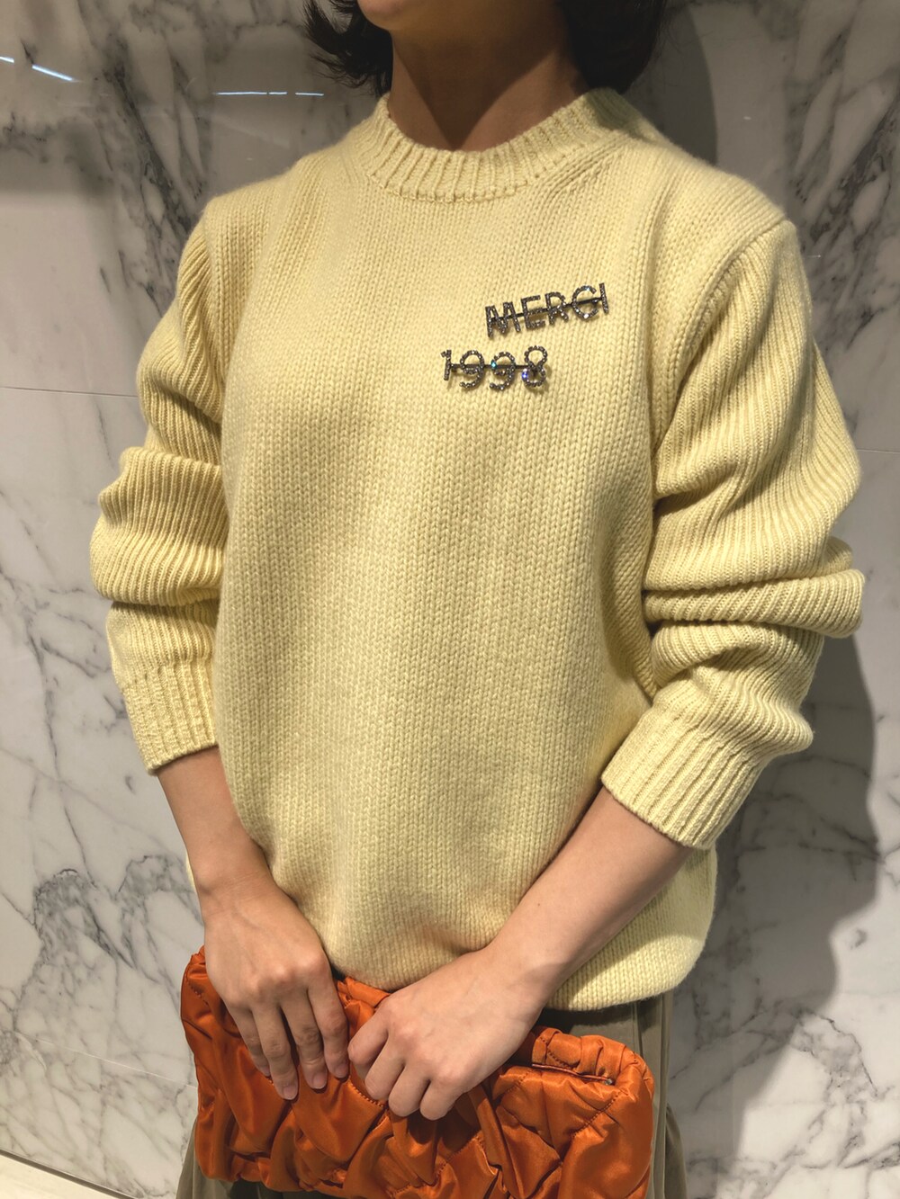 イエロー系のニット/セーター、オレンジ系のショルダーバッグ、グリーン系のスカートを着用したレディースの秋コーディネートの4枚目の写真