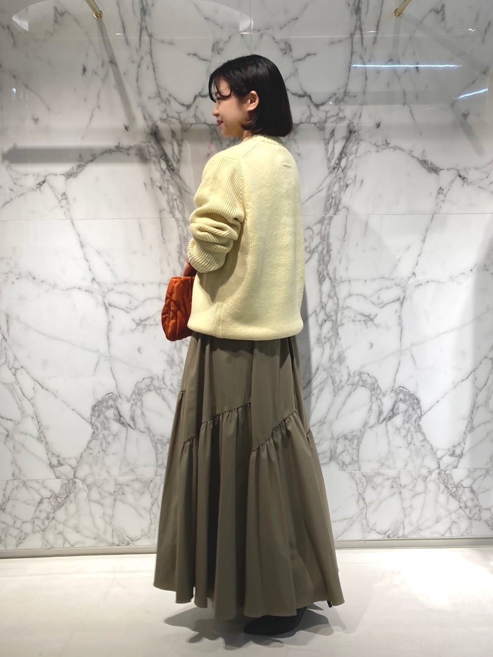イエロー系のニット/セーター、オレンジ系のショルダーバッグ、グリーン系のスカートを着用したレディースの秋コーディネートの2枚目の写真