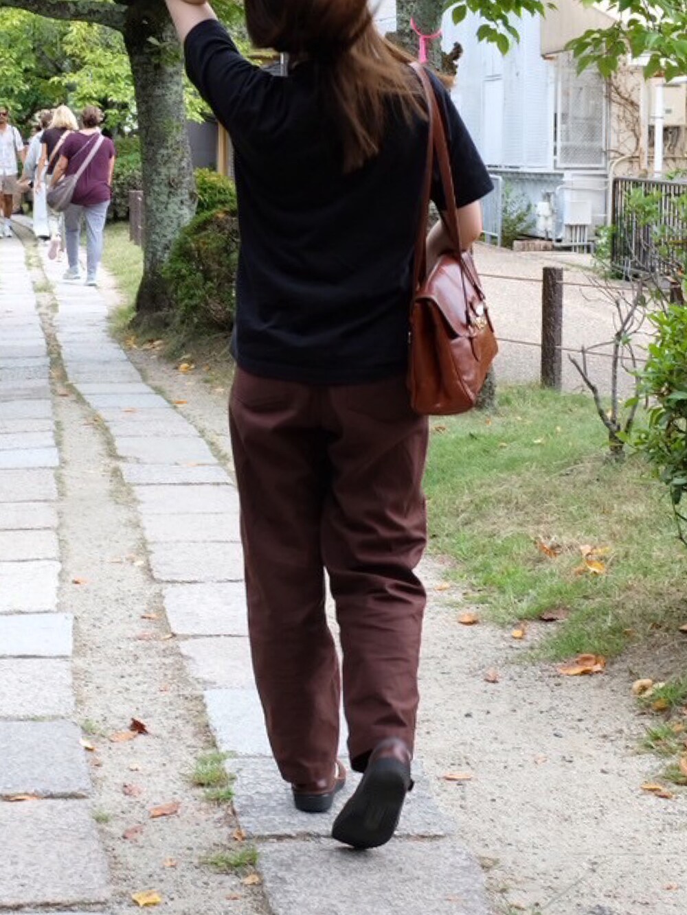 ブラック系のTシャツ/カットソー、ブラウン系のパンツ、ブラウン系のショルダーバッグを着用したレディースの秋コーディネートの2枚目の写真