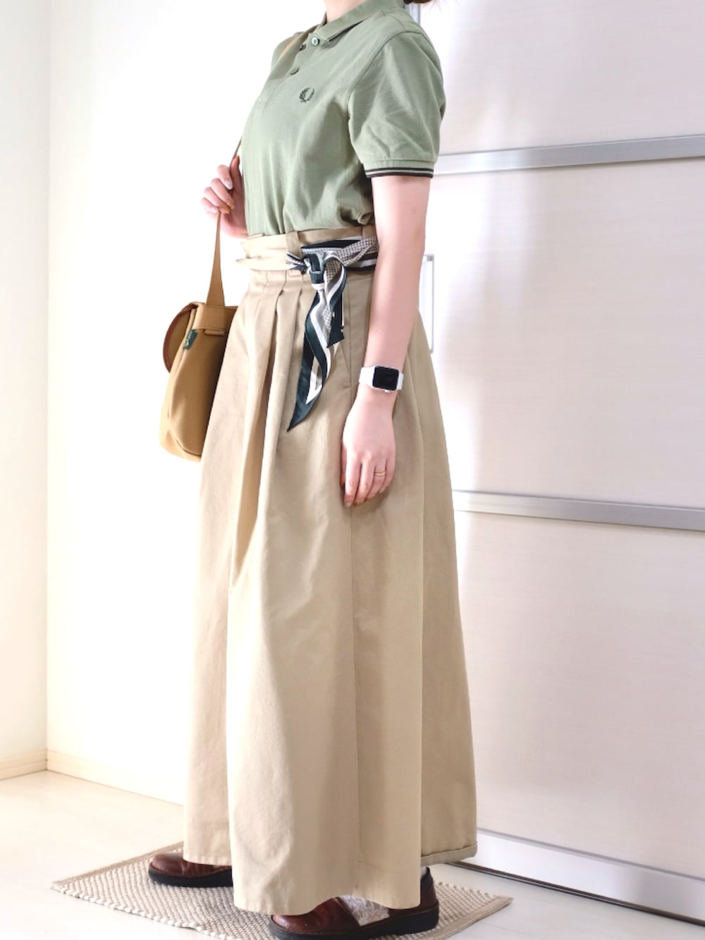 ベージュ系のショルダーバッグ、ベージュ系のスカート、グリーン系のポロシャツを着用したレディースの秋コーディネートの2枚目の写真