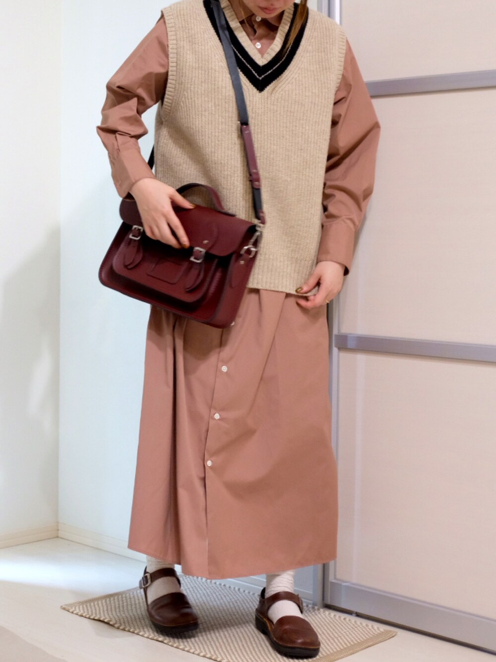 ベージュ系のベスト、ピンク系のシャツワンピース、レッド系のショルダーバッグを着用したレディースの秋コーディネートの3枚目の写真