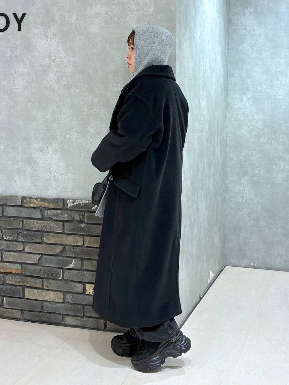 ブラック系のスニーカー、ブラック系のチェスターコート、ブラック系のデニムパンツを着用したレディースの冬コーディネートの6枚目の写真