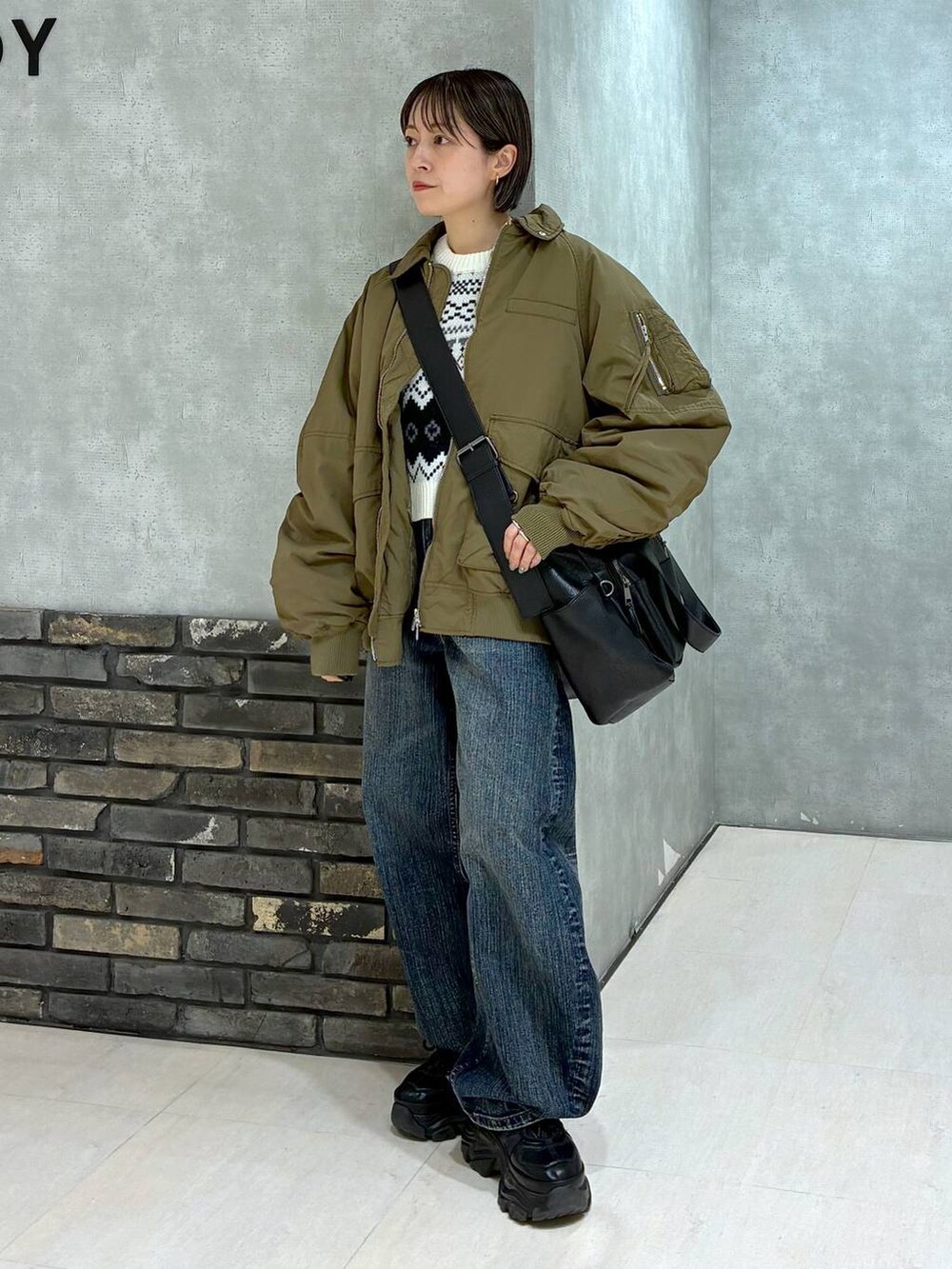 ブラック系のスニーカー、ブラック系のボストンバッグ、ブルー系のデニムパンツを着用したレディースの冬コーディネートの2枚目の写真