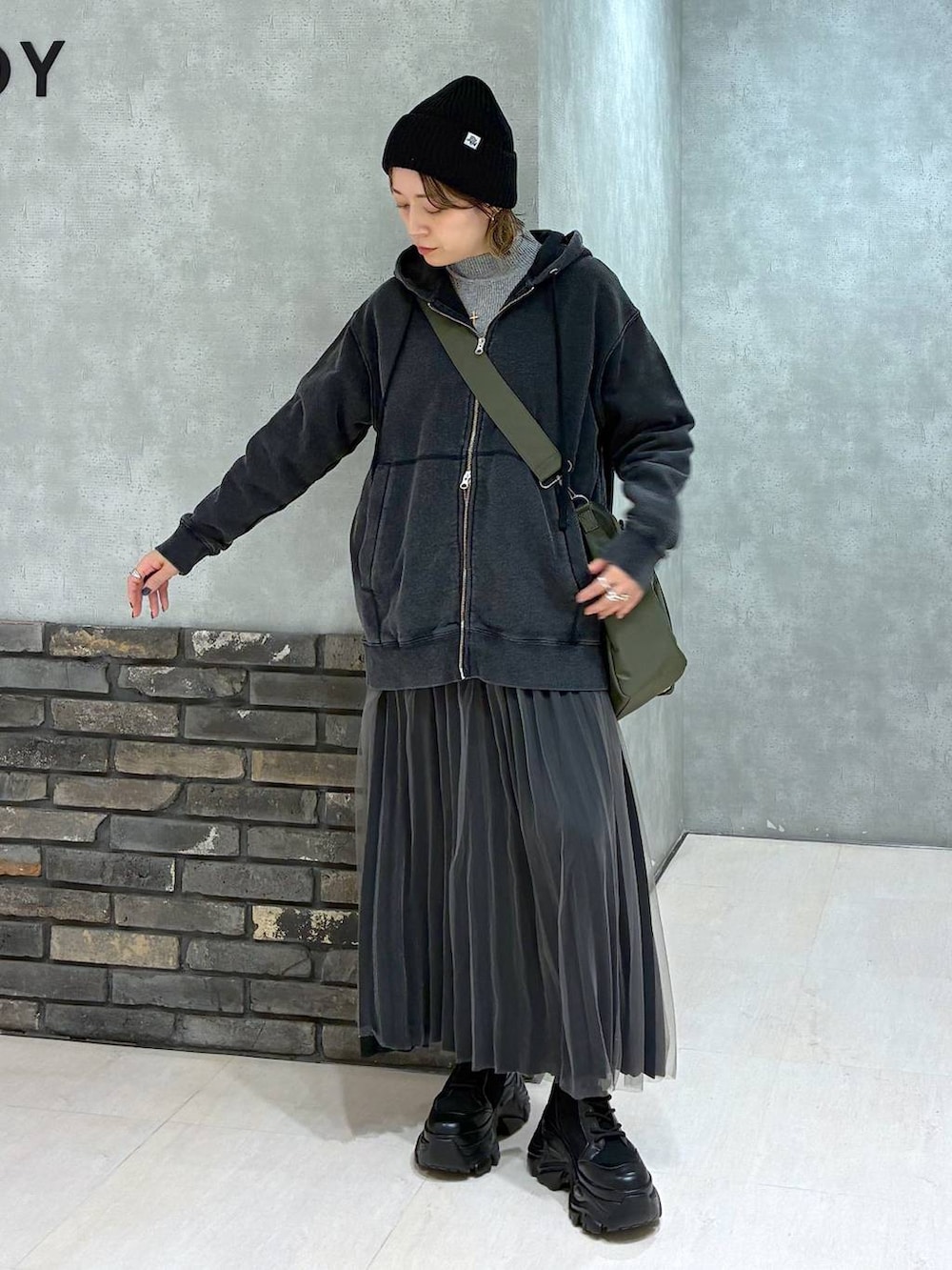 ブラック系のブーツ、グリーン系のボストンバッグ、ブラック系のパーカーを着用したレディースの秋コーディネートの2枚目の写真