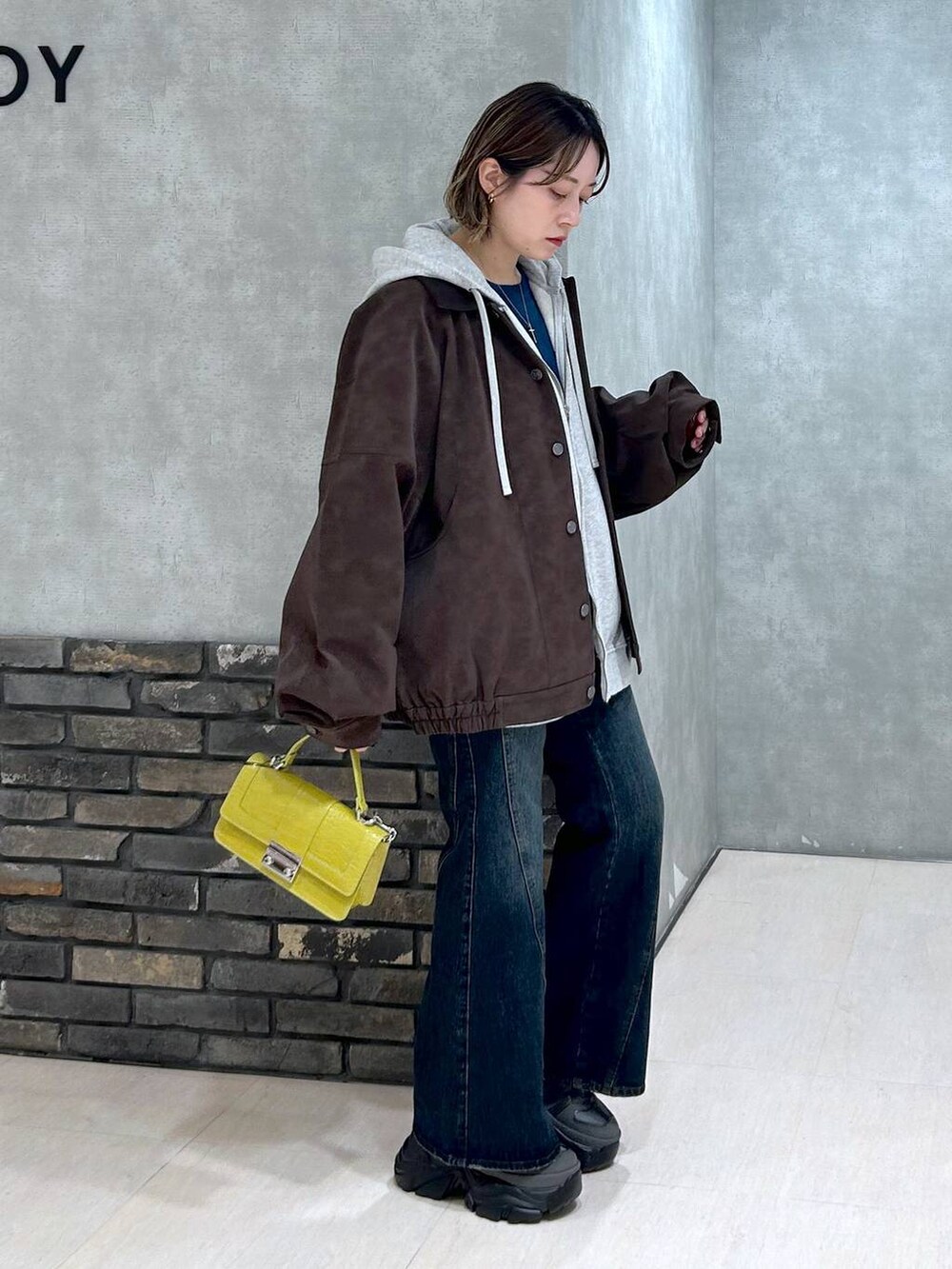 グレー系のスニーカー、ブルー系のデニムパンツ、イエロー系のハンドバッグを着用したレディースの秋コーディネートの2枚目の写真