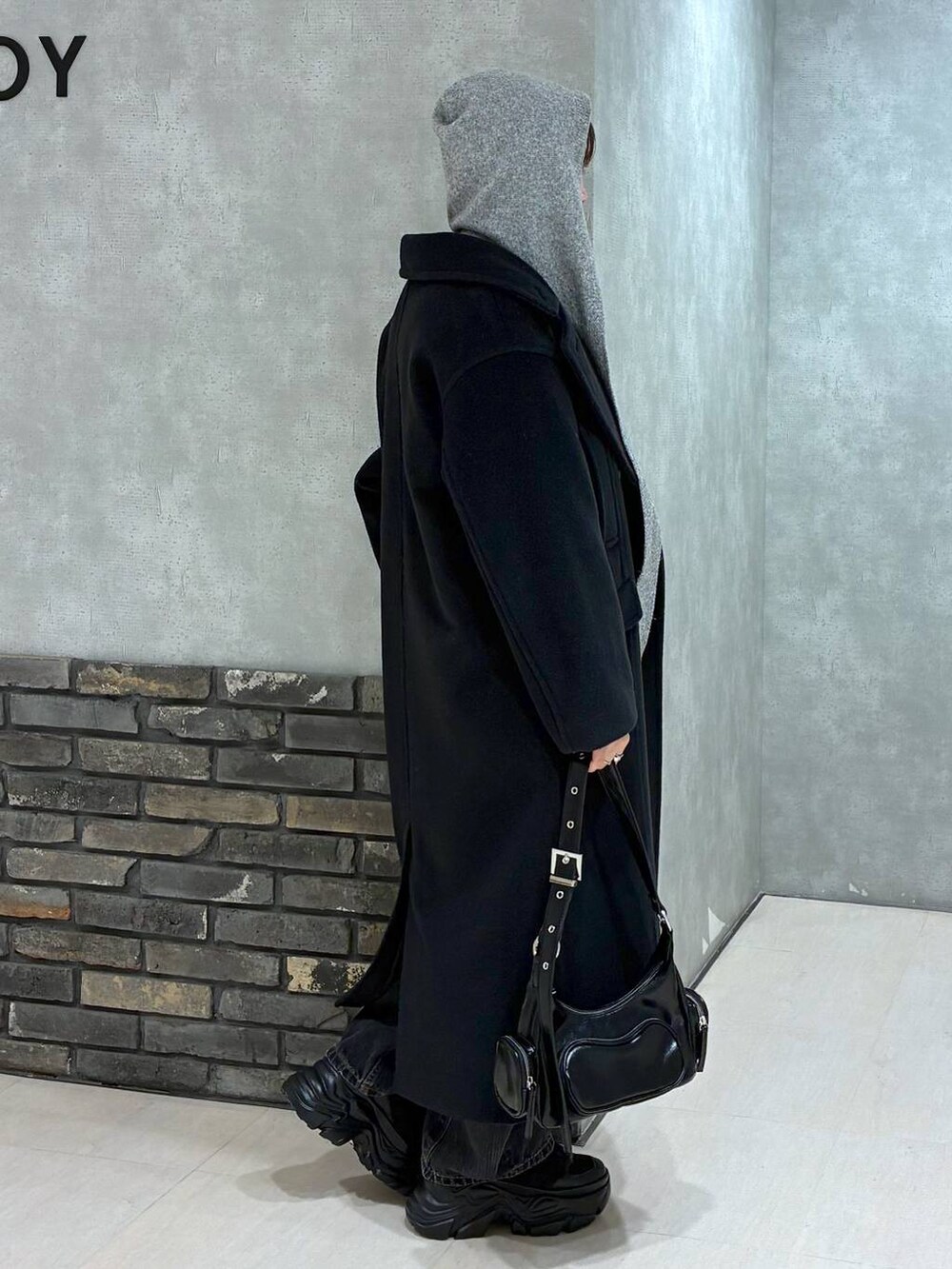 ブラック系のスニーカー、ブラック系のチェスターコート、ブラック系のデニムパンツを着用したレディースの冬コーディネートの3枚目の写真