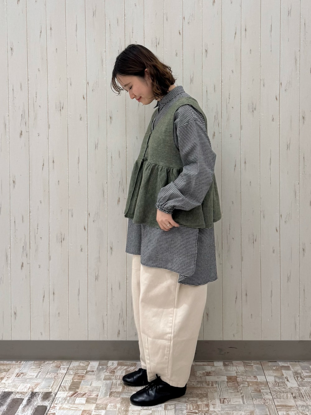 グリーン系のベスト、ブラック系のチュニック、ホワイト系のその他パンツを着用したレディースの春コーディネートの2枚目の写真