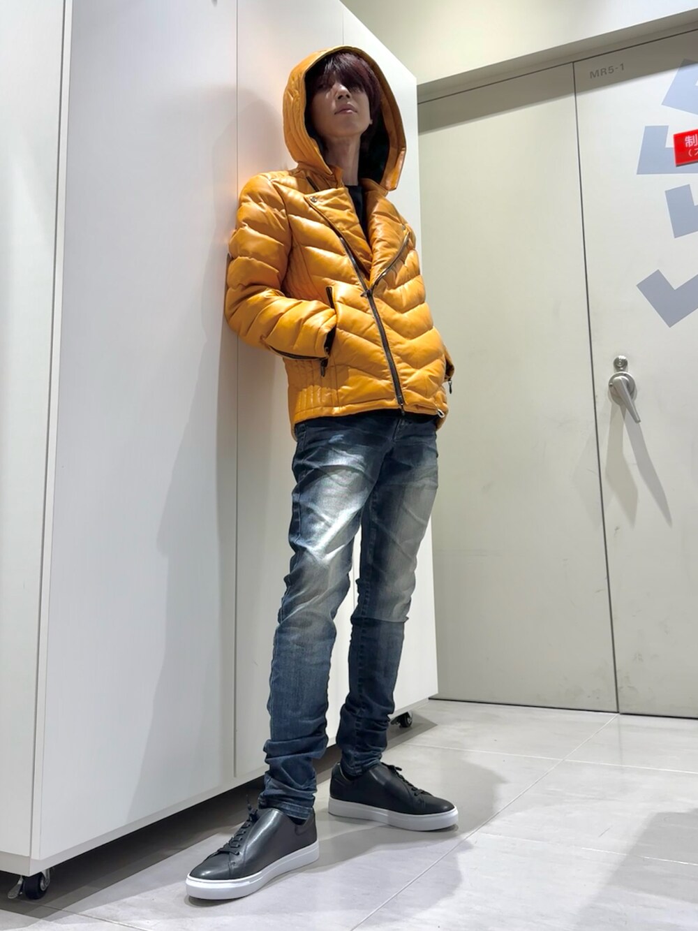 オレンジ系のダウンジャケット/コート、ブルー系のデニムパンツ、ブラック系のスニーカーを着用したメンズの秋コーディネートの4枚目の写真