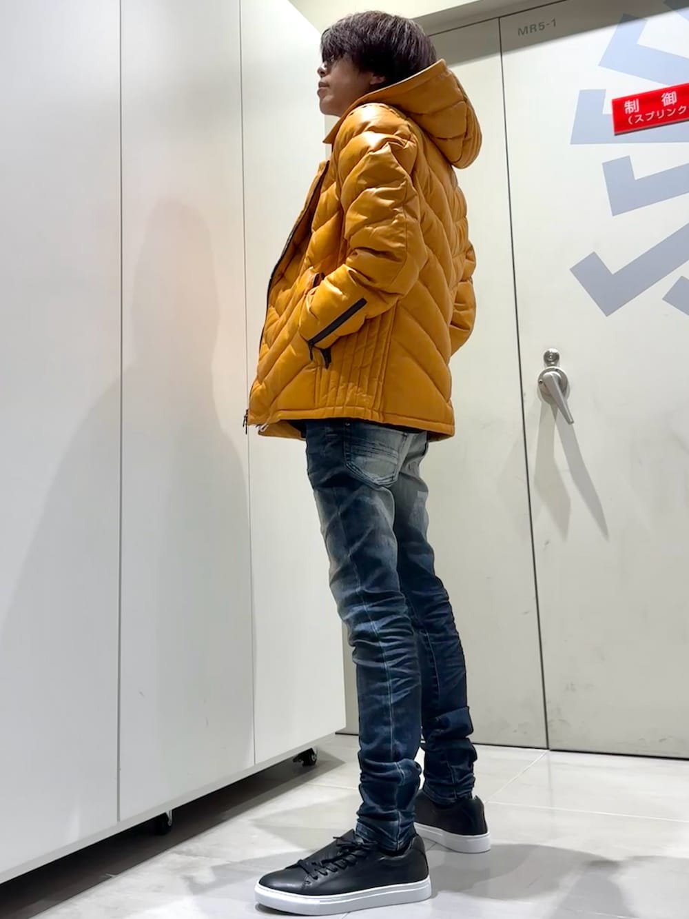 オレンジ系のダウンジャケット/コート、ブルー系のデニムパンツ、ブラック系のスニーカーを着用したメンズの秋コーディネートの2枚目の写真