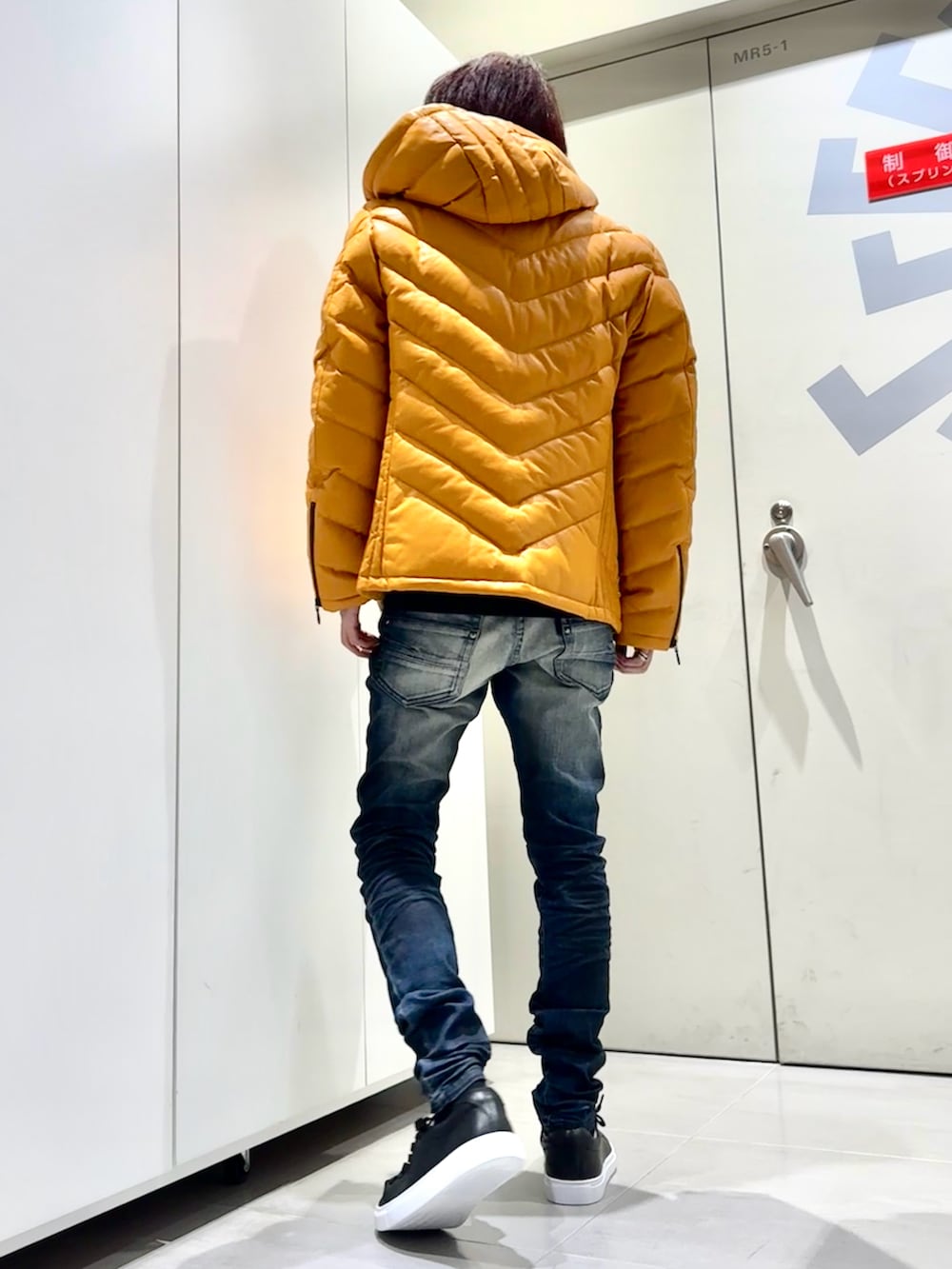 オレンジ系のダウンジャケット/コート、ブルー系のデニムパンツ、ブラック系のスニーカーを着用したメンズの秋コーディネートの3枚目の写真