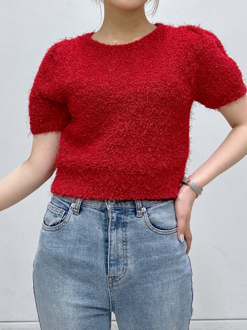 レッド系のニット/セーター、ブラック系のショルダーバッグ、ブルー系のデニムパンツを着用したレディースの夏コーディネートの3枚目の写真