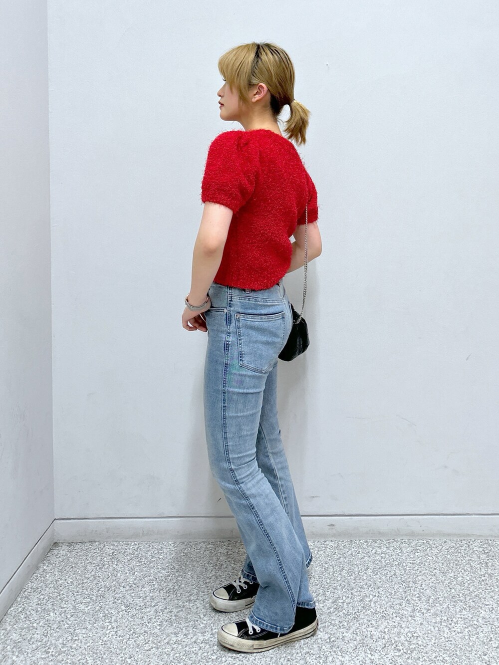 レッド系のニット/セーター、ブラック系のショルダーバッグ、ブルー系のデニムパンツを着用したレディースの夏コーディネートの2枚目の写真