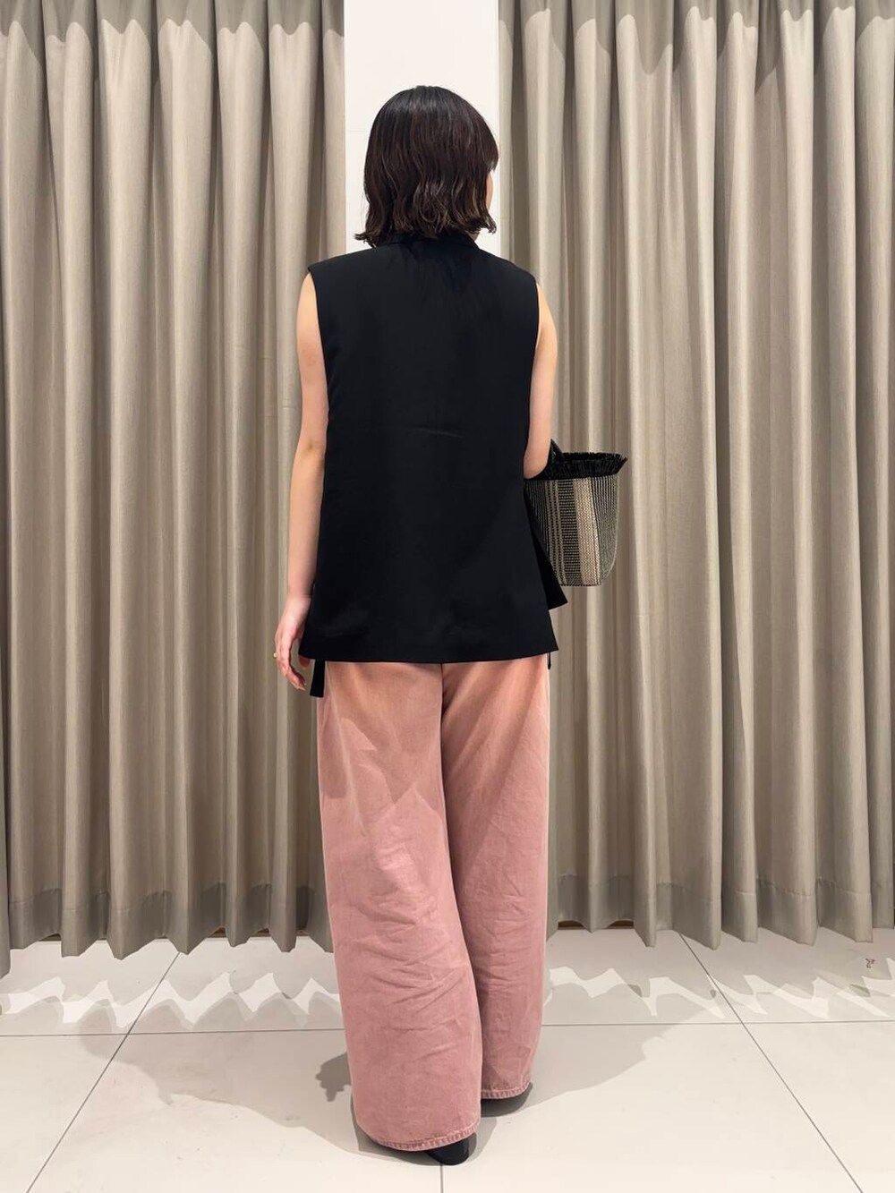 ピンク系のデニムパンツ、ブラック系のベスト、ブラック系のショルダーバッグを着用したレディースの春コーディネートの2枚目の写真