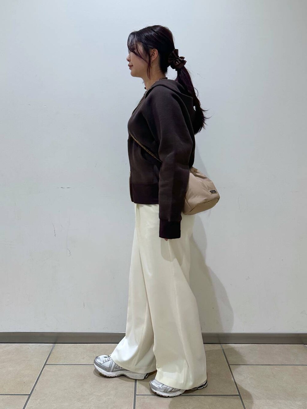 ブラウン系のパーカー、ベージュ系のショルダーバッグ、ホワイト系のスラックスを着用したレディースの冬コーディネートの2枚目の写真