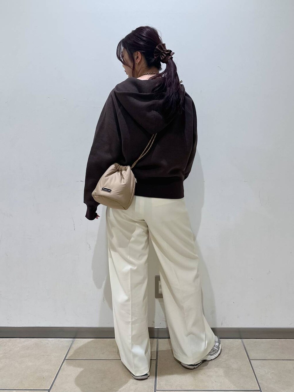 ブラウン系のパーカー、ベージュ系のショルダーバッグ、ホワイト系のスラックスを着用したレディースの冬コーディネートの3枚目の写真