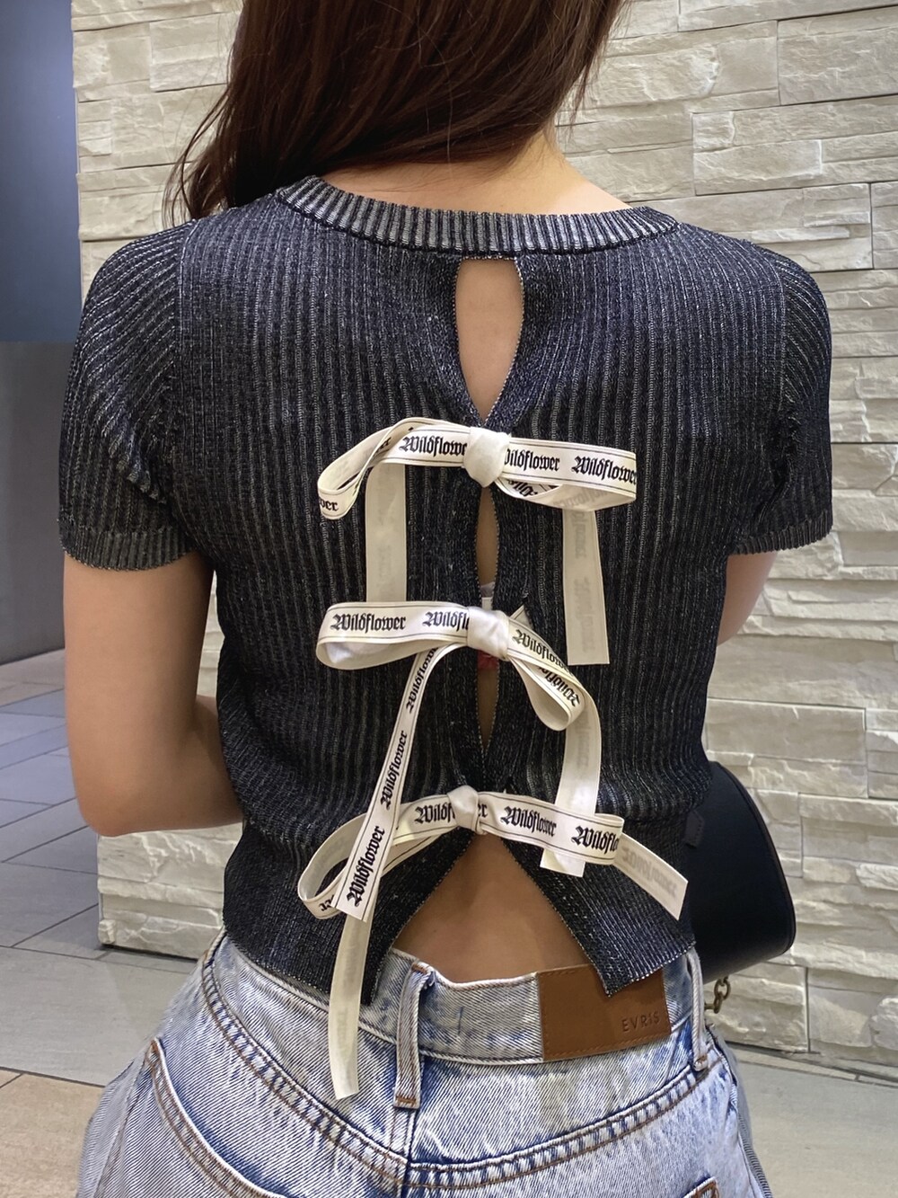 ブラック系のニット/セーター、ブルー系のデニムパンツ、その他のショルダーバッグを着用したレディースの夏コーディネートの4枚目の写真