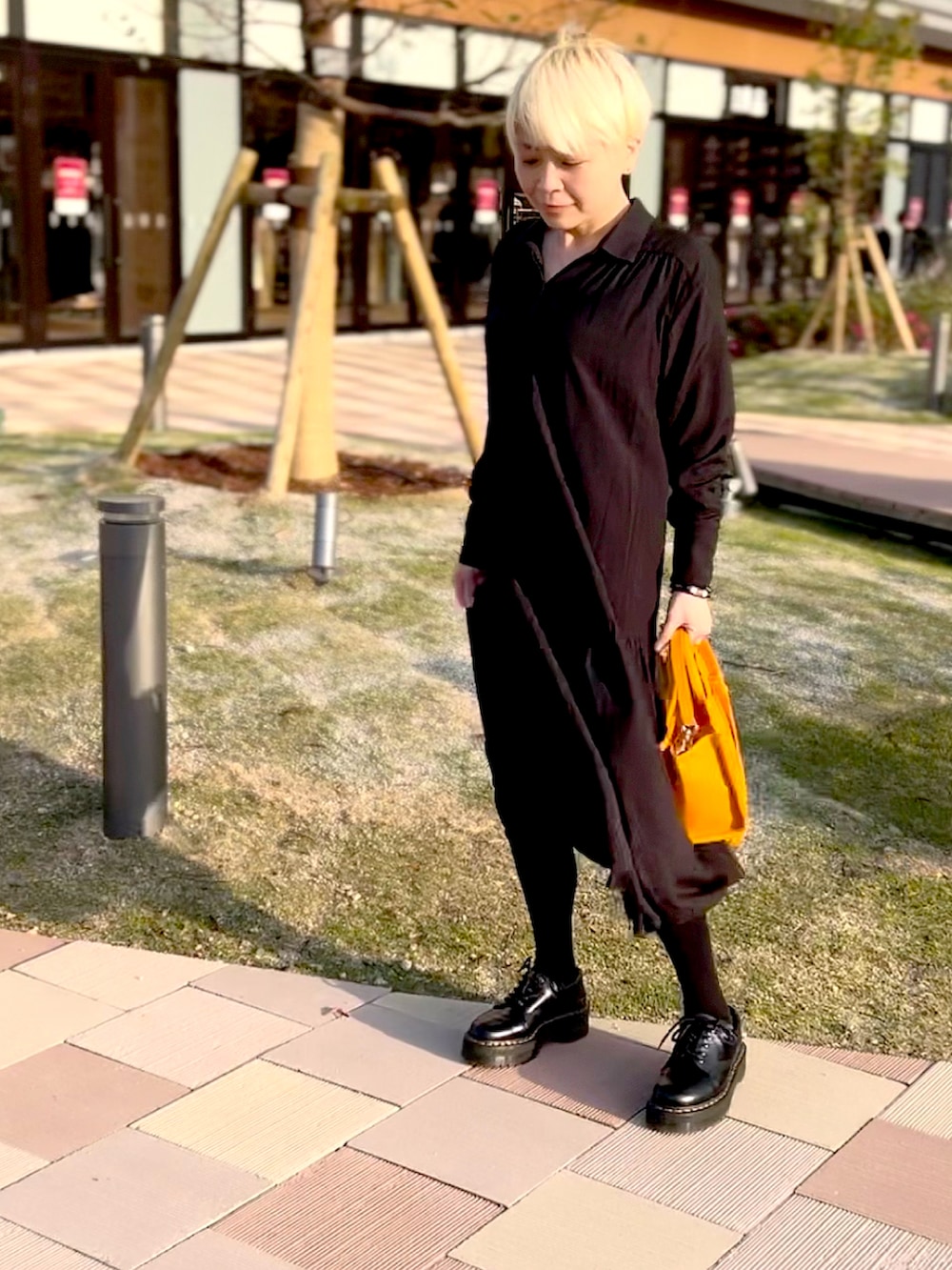 オレンジ系のトートバッグ、ブラック系のシャツワンピース、ブラック系のシューズを着用したレディースの春コーディネートの2枚目の写真