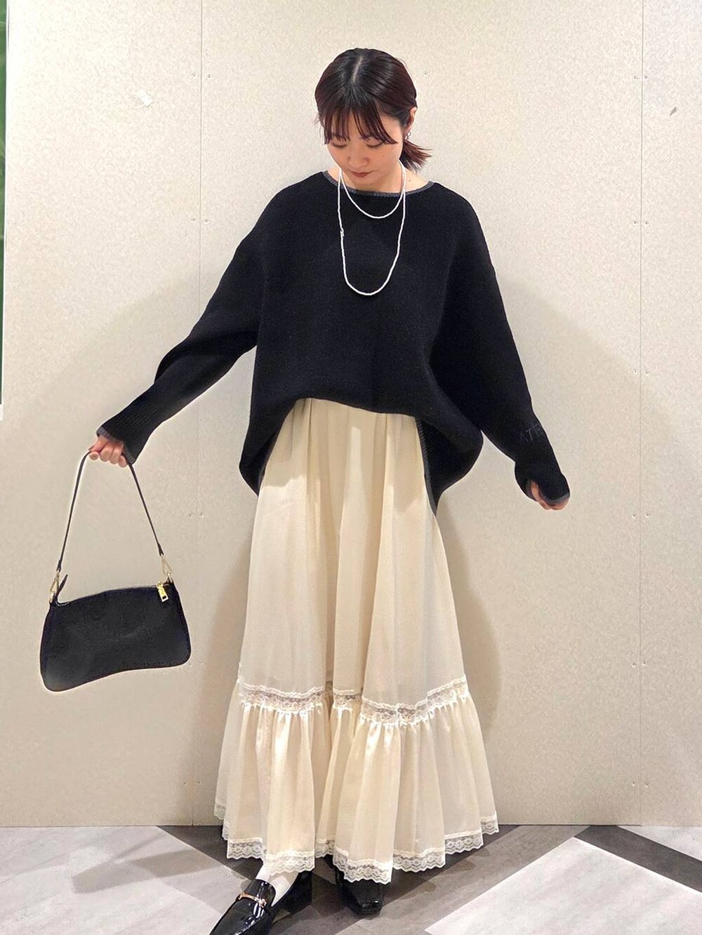 ブラック系のローファー、ブラック系のショルダーバッグ、ホワイト系のスカートを着用したレディースの秋コーディネートの2枚目の写真