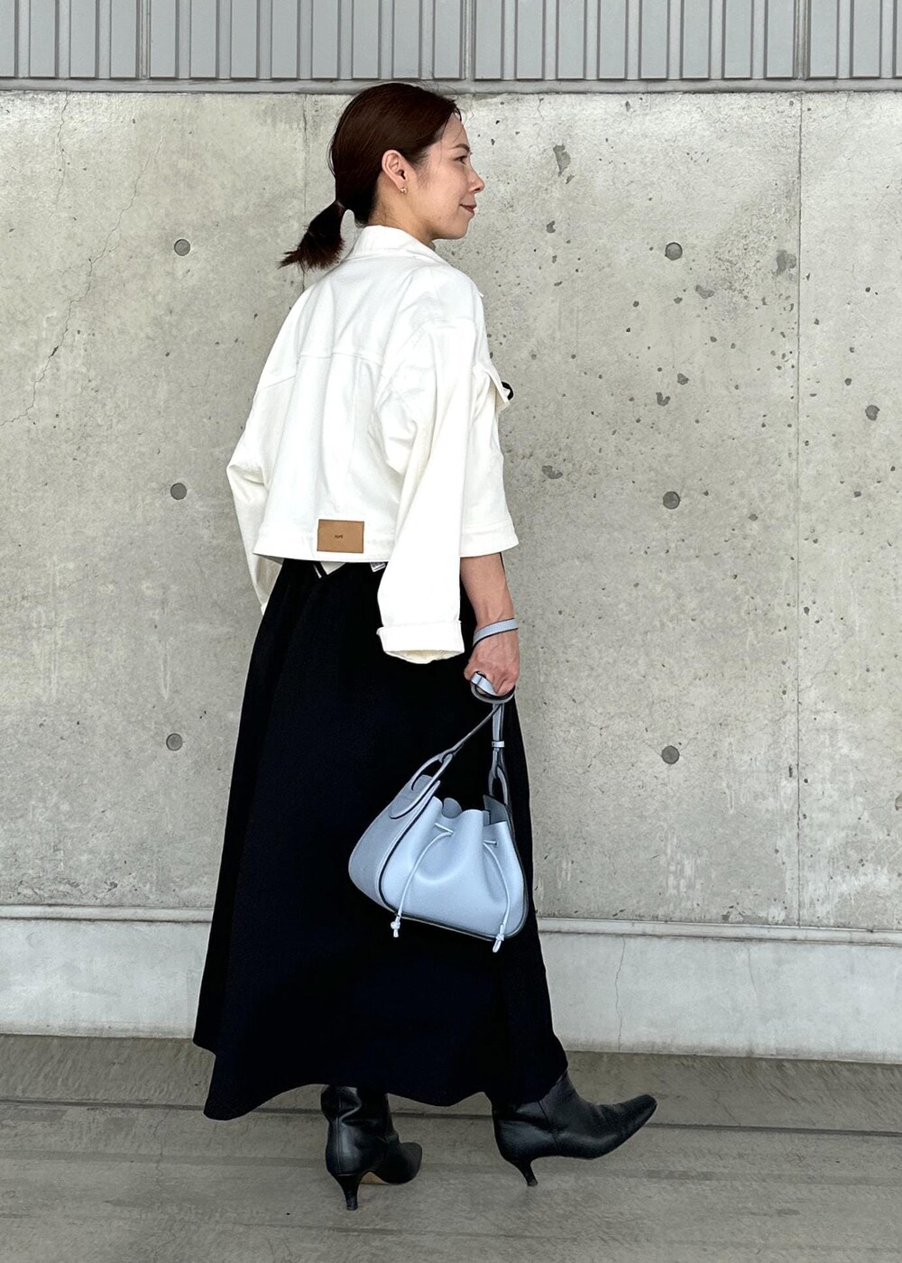 ホワイト系のデニムジャケット、ブルー系のハンドバッグ、ブラック系のワンピースを着用したレディースの秋コーディネートの2枚目の写真