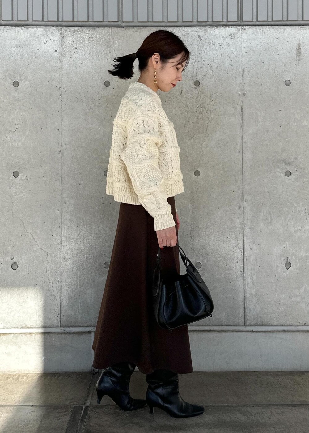 ブラック系のハンドバッグ、ブラウン系のスカート、ホワイト系のニット/セーターを着用したレディースの冬コーディネートの4枚目の写真