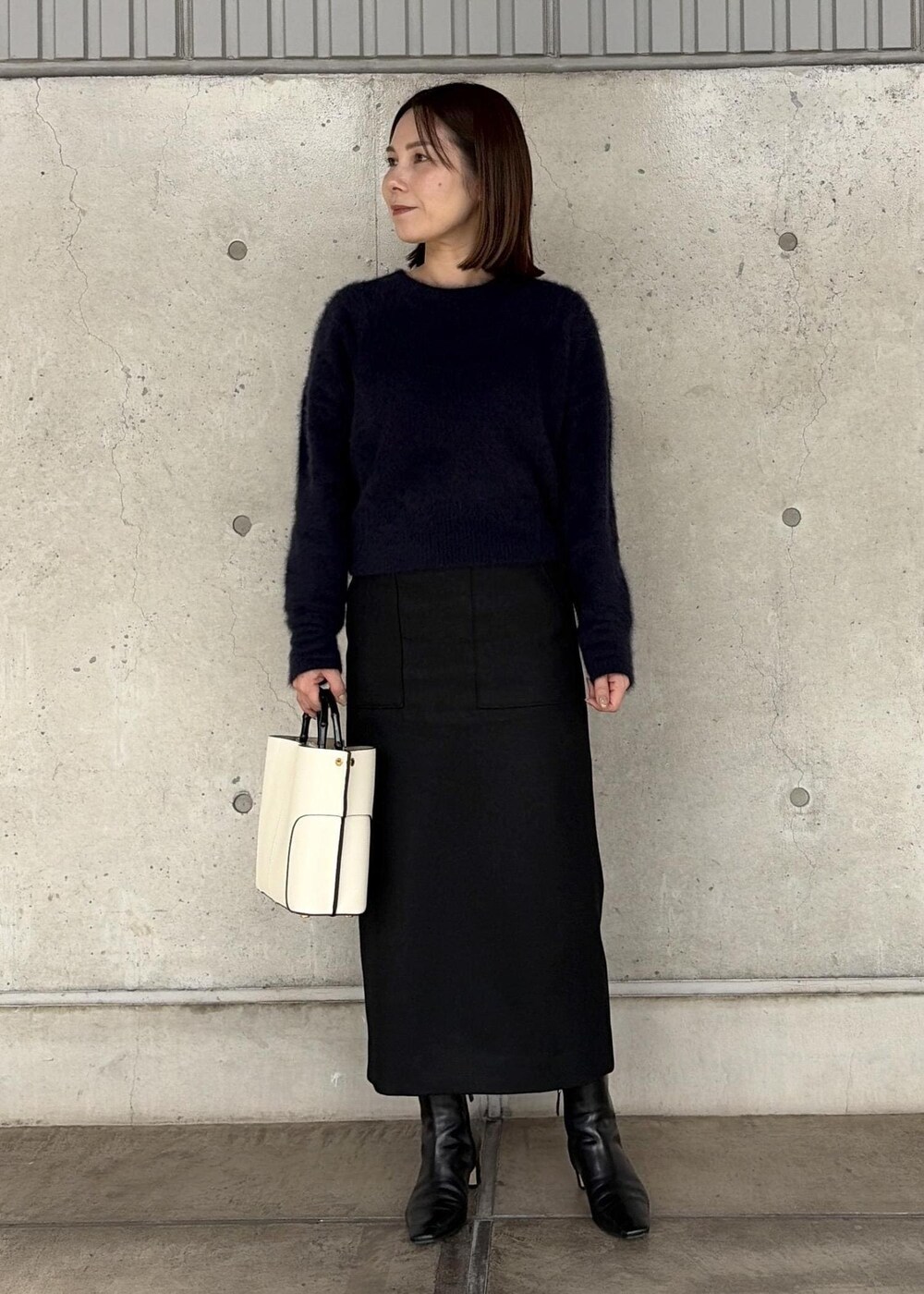 ホワイト系のハンドバッグ、ブラック系のブーツ、ブラック系のスカートを着用したレディースの秋コーディネートの7枚目の写真
