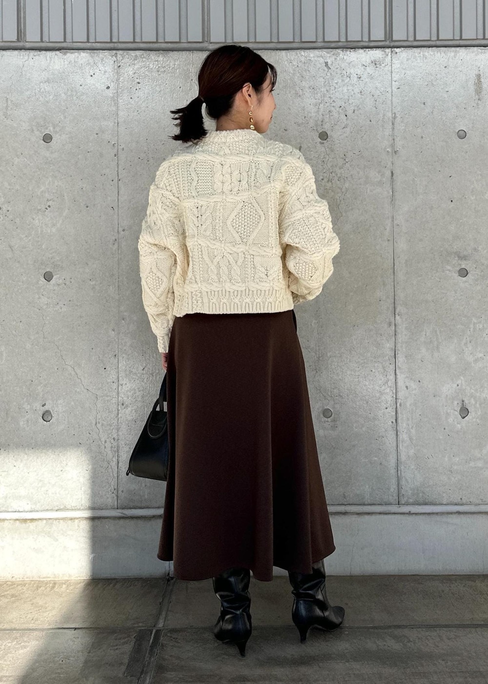 ブラック系のハンドバッグ、ブラウン系のスカート、ホワイト系のニット/セーターを着用したレディースの冬コーディネートの3枚目の写真