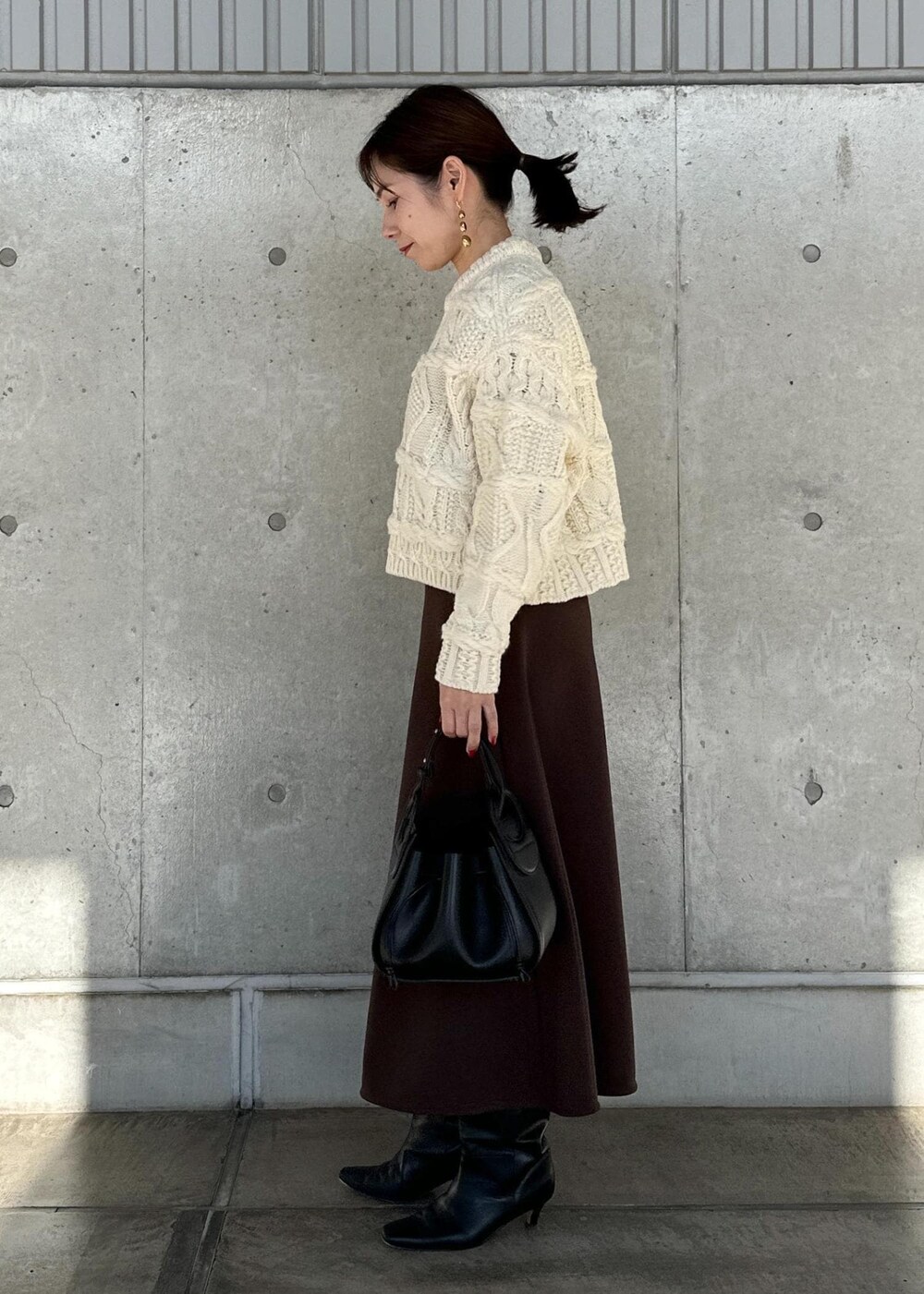 ブラック系のハンドバッグ、ブラウン系のスカート、ホワイト系のニット/セーターを着用したレディースの冬コーディネートの2枚目の写真