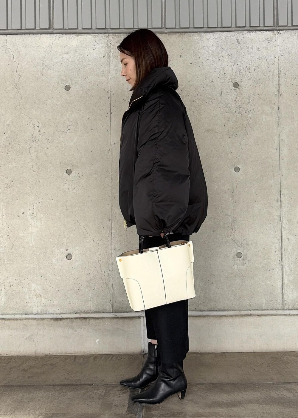 ホワイト系のハンドバッグ、ブラック系のブーツ、ブラック系のスカートを着用したレディースの秋コーディネートの2枚目の写真