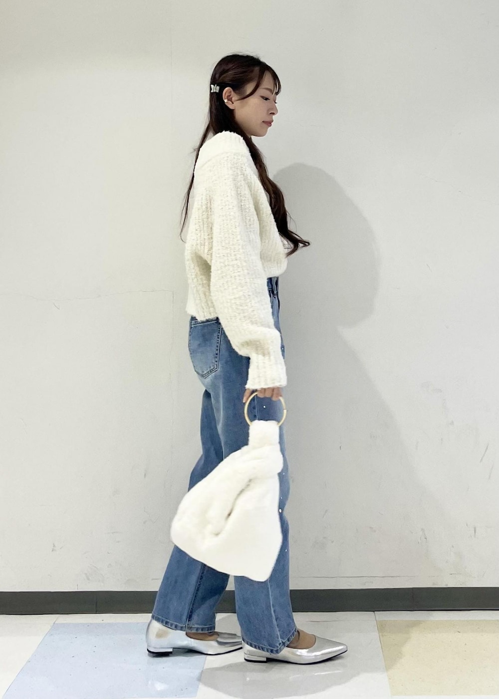 ホワイト系のハンドバッグ、ブルー系のデニムパンツ、シルバー系のパンプスを着用したレディースの秋コーディネートの2枚目の写真