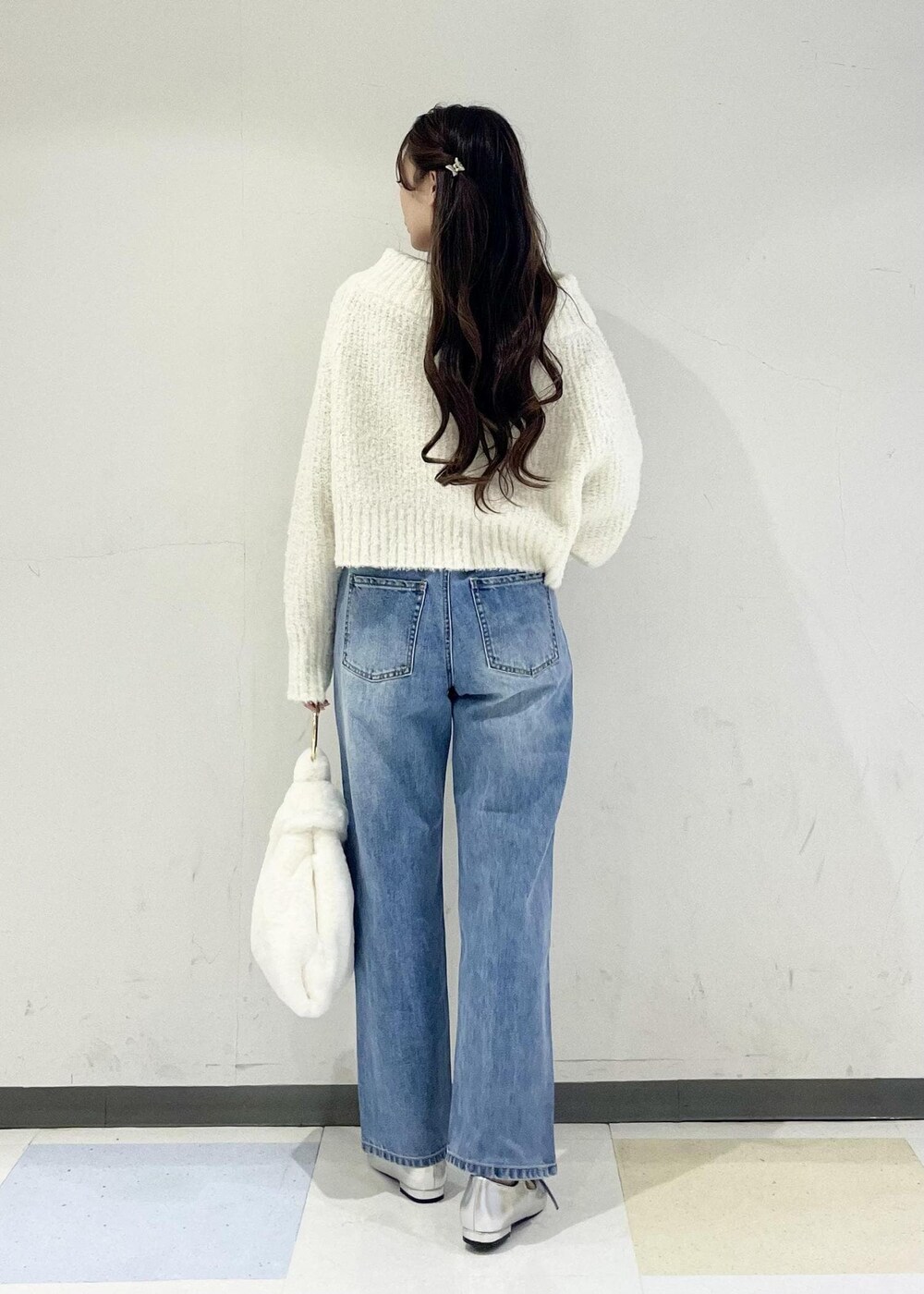 ホワイト系のハンドバッグ、ブルー系のデニムパンツ、シルバー系のパンプスを着用したレディースの秋コーディネートの3枚目の写真