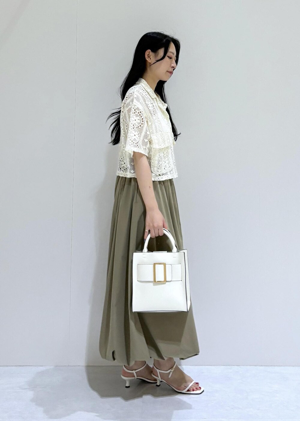 ホワイト系のサンダル、ホワイト系のハンドバッグ、グリーン系のスカートを着用したレディースの夏コーディネートの2枚目の写真
