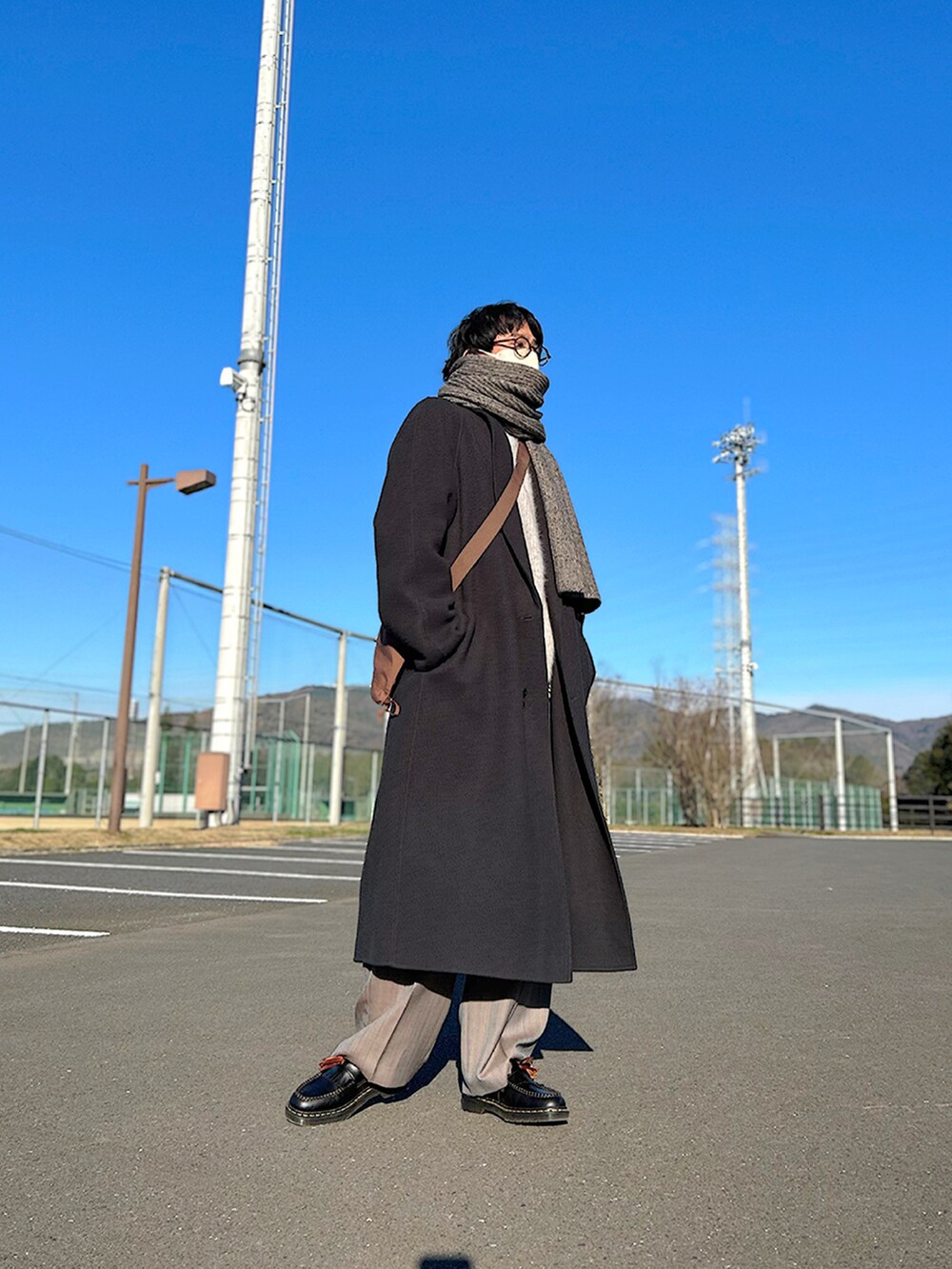 グレー系のチェスターコート、グレー系のニット/セーター、ブラウン系のショルダーバッグを着用したメンズの冬コーディネートの2枚目の写真