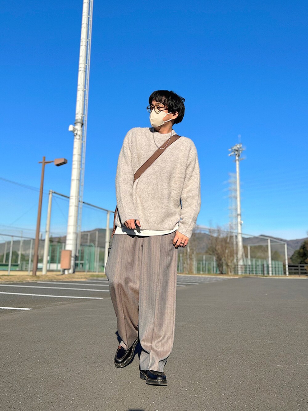 グレー系のチェスターコート、グレー系のニット/セーター、ブラウン系のショルダーバッグを着用したメンズの冬コーディネートの3枚目の写真