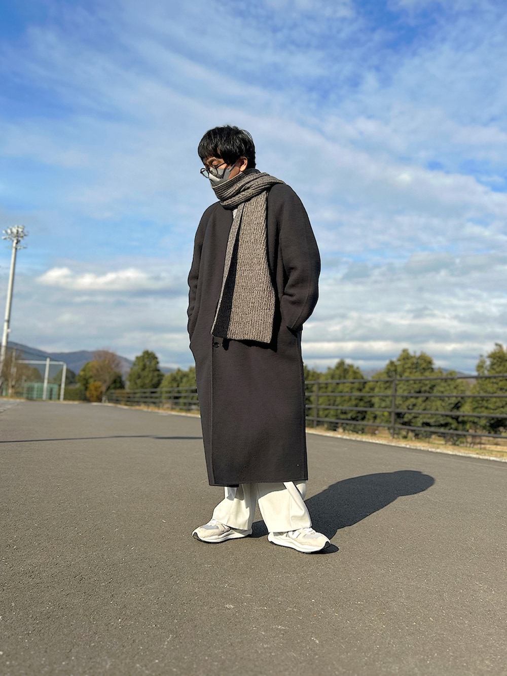 グレー系のチェスターコート、グレー系のニット/セーター、ブラック系のショルダーバッグを着用したメンズの冬コーディネートの2枚目の写真