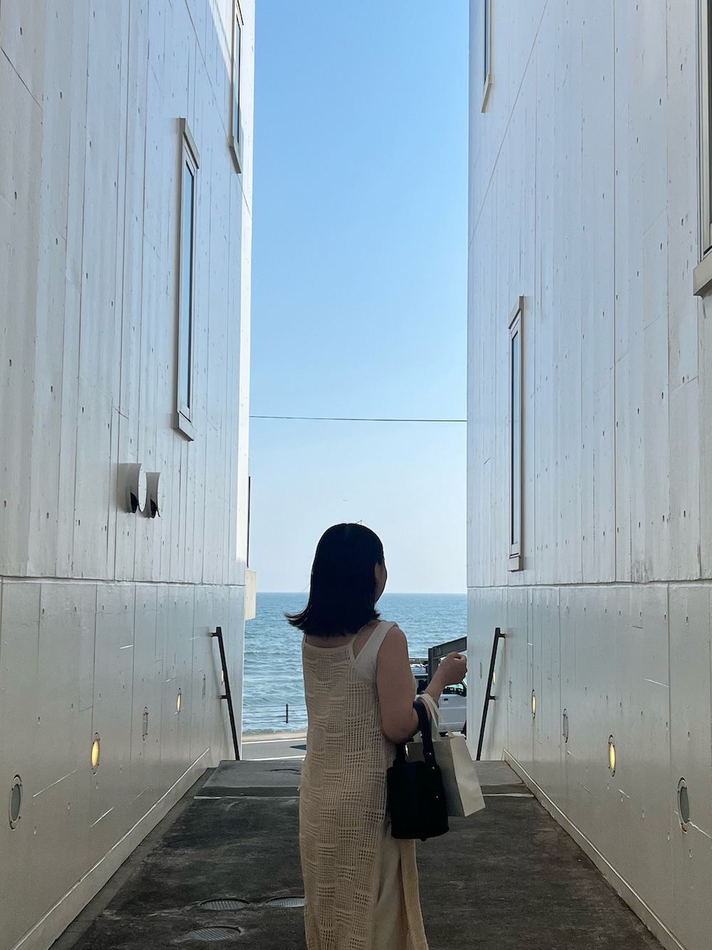 ホワイト系のワンピース、ブラック系のハンドバッグを着用したレディースの夏コーディネートの2枚目の写真