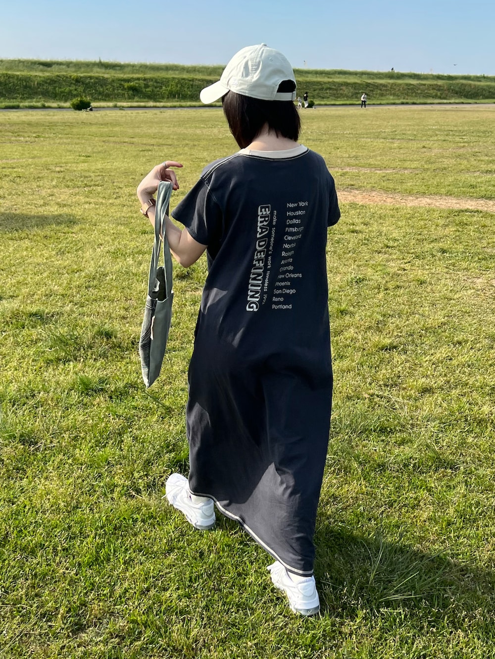 グレー系のワンピース、グレー系のトートバッグ、ホワイト系のスニーカーを着用したレディースの春コーディネートの2枚目の写真