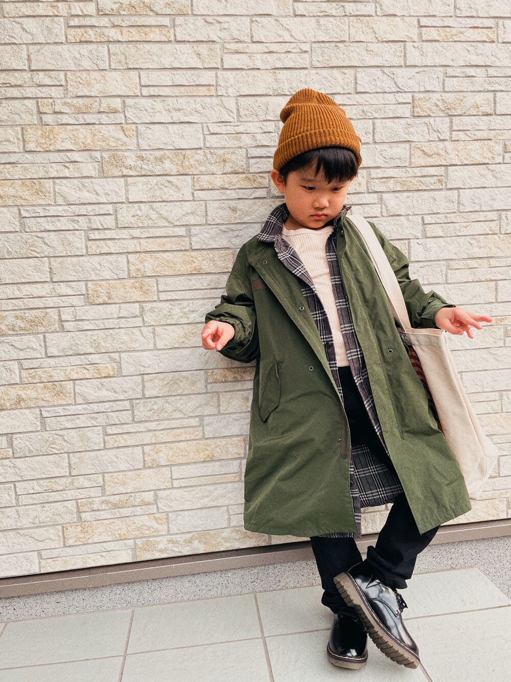 グリーン系のモッズコート、グレー系のシャツワンピース、ブラック系のデニムパンツを着用したキッズの秋コーディネートの2枚目の写真