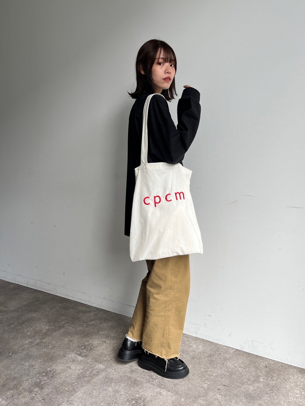 ブラック系のTシャツ/カットソー、ベージュ系のチノパンツ、ホワイト系のトートバッグを着用したレディースの夏コーディネートの2枚目の写真