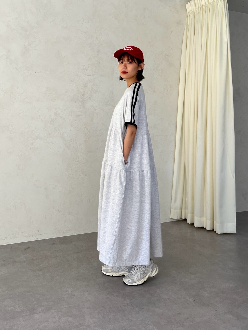グレー系のワンピース、レッド系のキャップを着用したレディースの春コーディネートの3枚目の写真