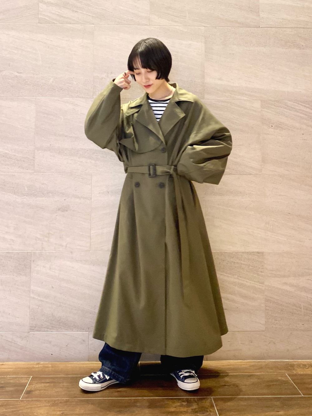 グリーン系のトレンチコート、ブラック系のショルダーバッグ、ブルー系のデニムパンツを着用したレディースの秋コーディネートの2枚目の写真