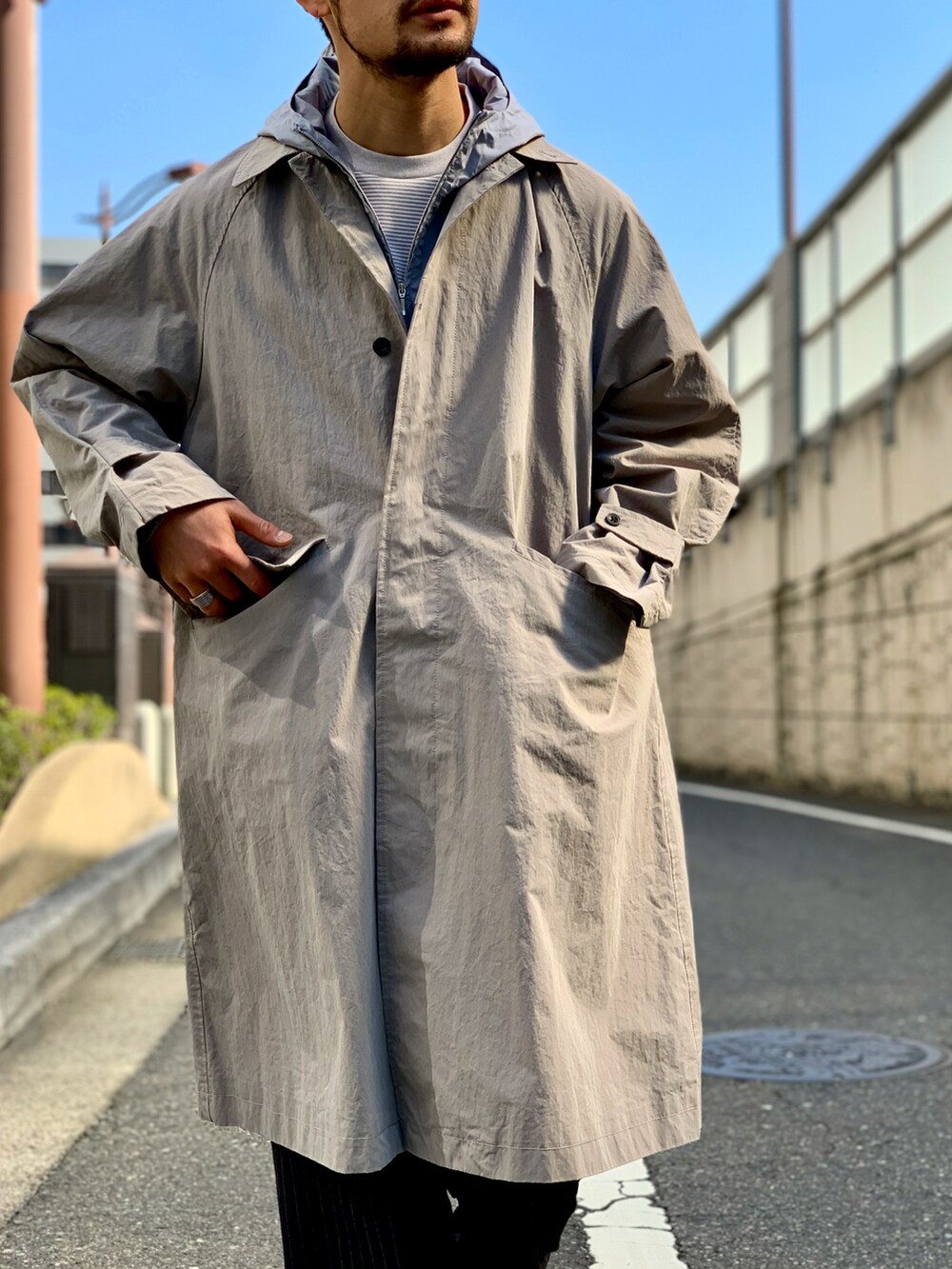 ブルー系のマウンテンパーカー、グレー系のステンカラーコート、ブラック系のスラックスを着用したメンズの春コーディネートの3枚目の写真