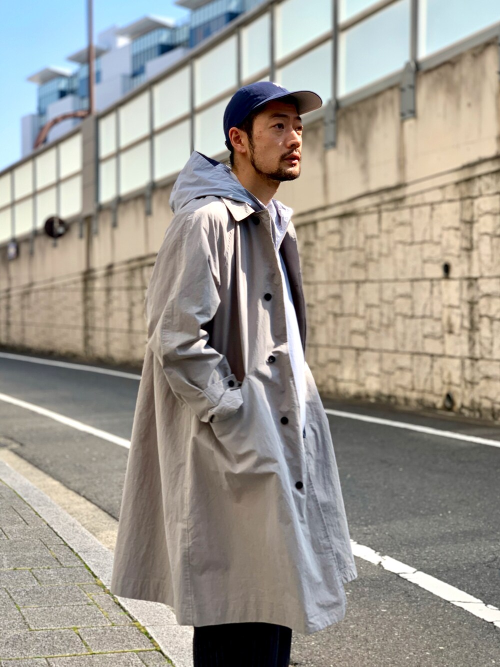 ブルー系のマウンテンパーカー、グレー系のステンカラーコート、ブラック系のスラックスを着用したメンズの春コーディネートの2枚目の写真