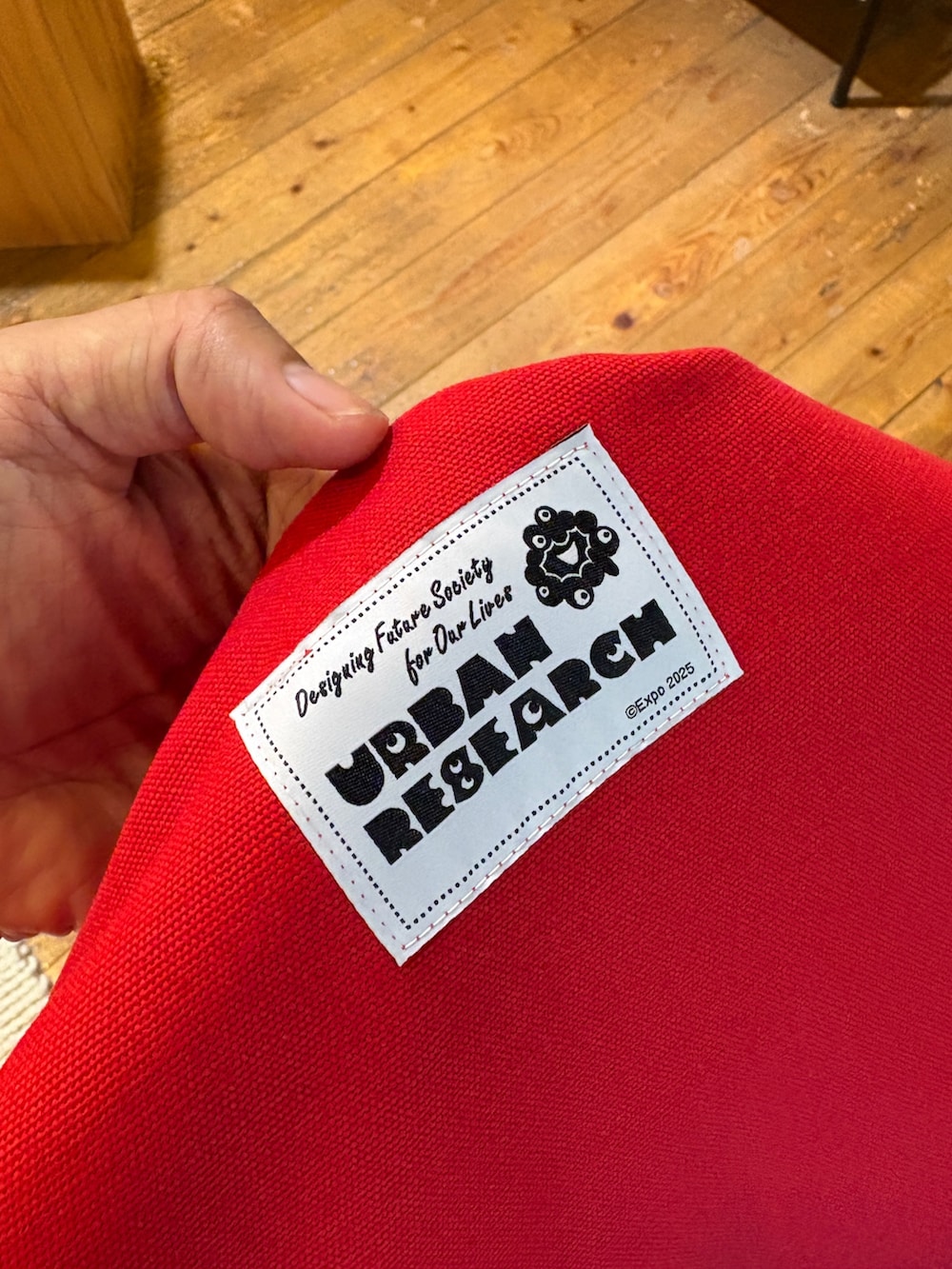 レッド系のトートバッグ、その他のデニムパンツ、ベージュ系のTシャツ/カットソーを着用したメンズの夏コーディネートの4枚目の写真