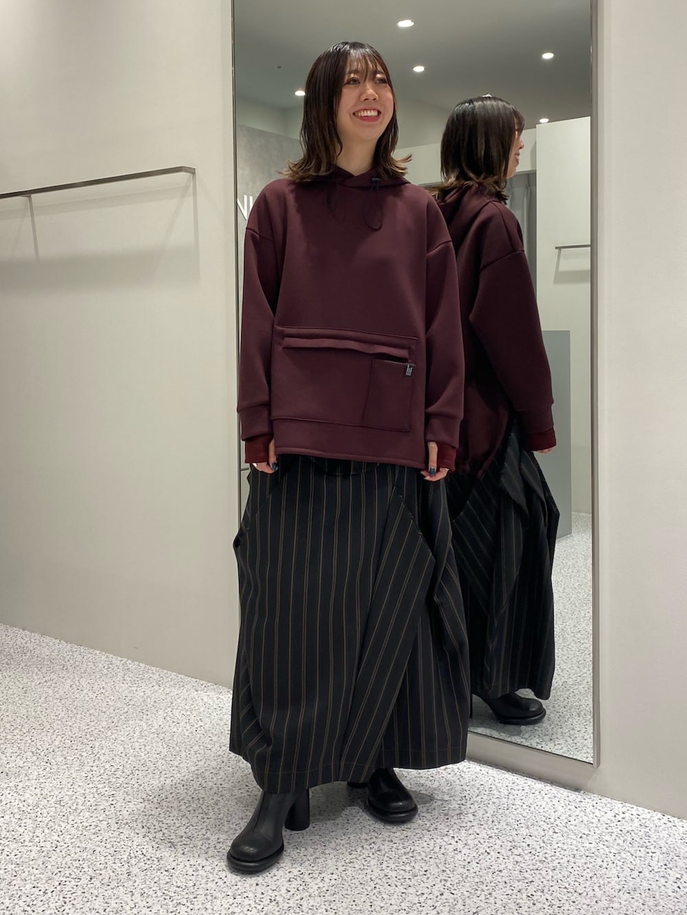 ブラウン系のパーカー、ブラック系のスカート、ブラック系のブーツを着用したレディースの秋コーディネートの2枚目の写真