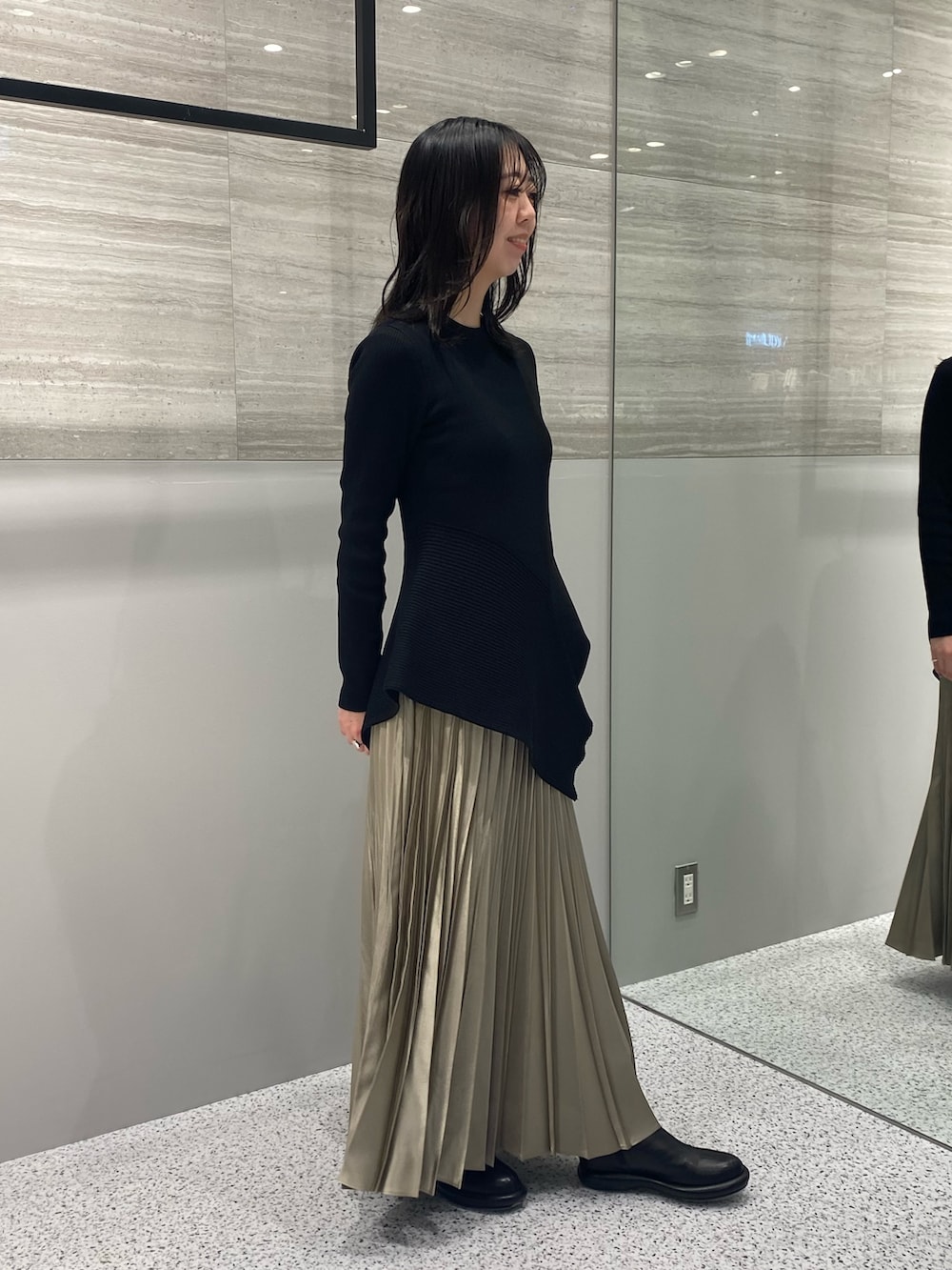 ブラック系のニット/セーター、ベージュ系のスカート、ブラック系のブーツを着用したレディースの春コーディネートの3枚目の写真