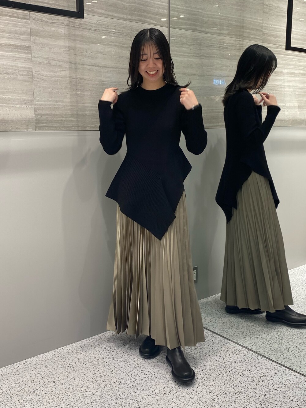 ブラック系のニット/セーター、ベージュ系のスカート、ブラック系のブーツを着用したレディースの春コーディネートの2枚目の写真